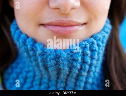 Close-up shot of a young female's smiling lips wearing a blue wool scarf around her neck. Stock Photo
