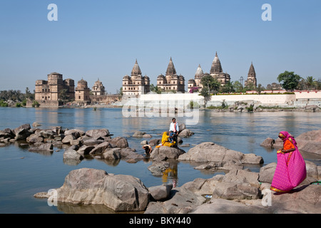 People bathing in the Petwa river.On the background the Royal cenotaphs. Orchha. Madhya Pradesh. India Stock Photo