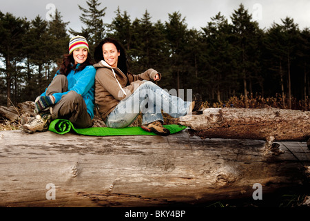 Two beautiful women smile while enjoying the sunset at La Push Beach, from a drift log. Stock Photo
