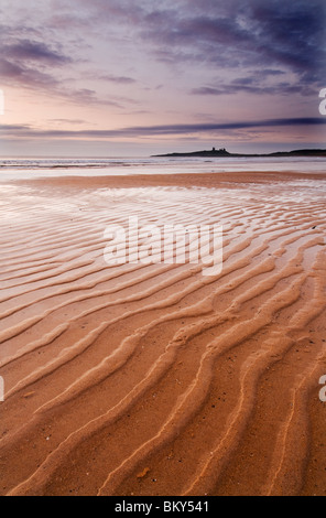 Ripples in the sand with Dunstanburgh Castle in the distance at Dawn Stock Photo