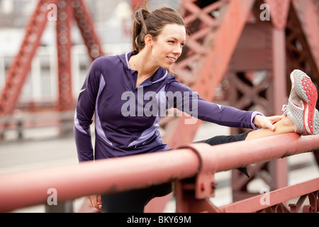 An athletic female in a purple jacket stretching along a bridge in Portland, Oregon.