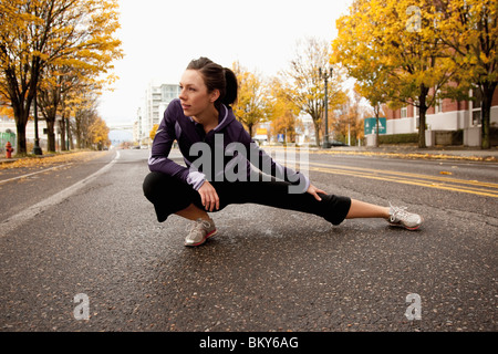An athletic female in a purple jacket stretching along a deserted street in Portland, Oregon.