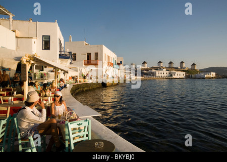 People sitting in restaurants and bars directly at sea, windmills in background, Little Venice, Mykonos-Town, Mykonos, Greece Stock Photo