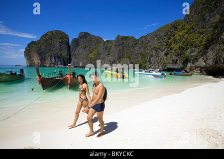 A young couple walking over the beach, anchored boats in background, Maya Bay, a beautiful scenic lagoon, famous for the Hollywo Stock Photo