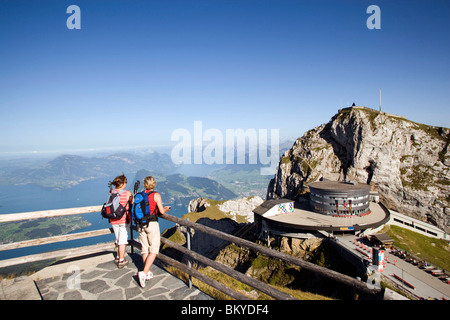 Two female hikers standing on vantage point looking to Hotel Bellevue in front of mount Esel (2118 m), panoramic view over Lake Stock Photo