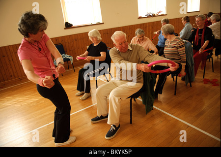 A group of fit active senior citizens participating in low-impact chair aerobics class in a small village hall in west wales UK Stock Photo