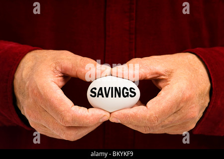 Man holds white egg with Savings written on it, symbolizing the fragility of money matters; the proverbial 'nest egg.' Stock Photo