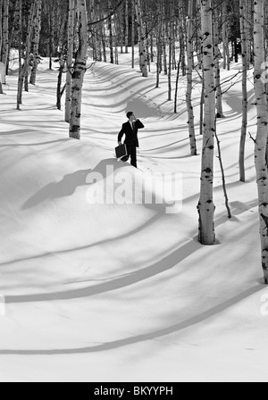 black and white monochrome image of a businessman carrying briefcase and cell phone lost in the snow and trees Stock Photo