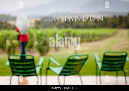 Domaine Chandon winery with green chairs on rainy patio, woman with umbrella, overlooking vines, bushes, trees and hills. Stock Photo