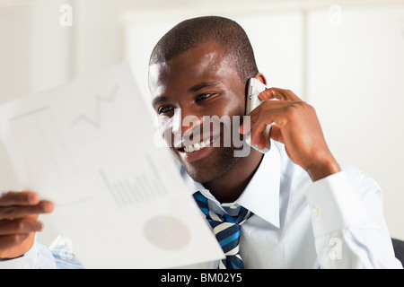 young adult afro-american businessman examining charts and talking on the phone Stock Photo