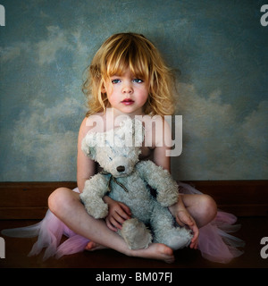 A young girl lost in thoughts holding a teddy and wearing a ballerina tutu Stock Photo