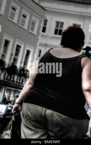 An over weight woman walking along a street in a town with her back to the camera Stock Photo