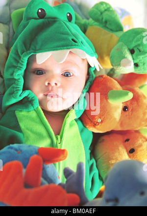 Closeup of a newborn baby with blue eyes in a dinosaur costume surrounded in dinosaur stuffed animals. Stock Photo