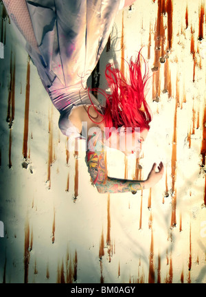 A woman with bright hair, a tattered dress, and lots of tattoos hangs upside-down like she is falling. Stock Photo