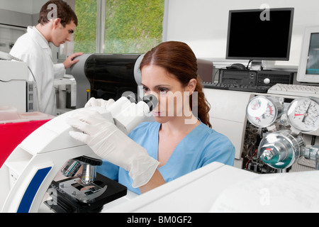 Female lab technician analyzing a sample through a microscope Stock Photo