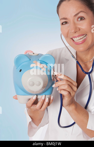 Female doctor examining a piggy bank with a stethoscope Stock Photo