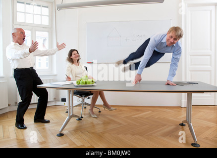 Businessman jumping over table Stock Photo