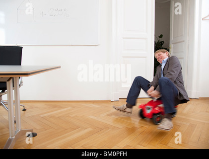 Businessman riding toy car in office Stock Photo