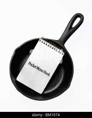 black cast iron fry pan with note book on white background Stock Photo