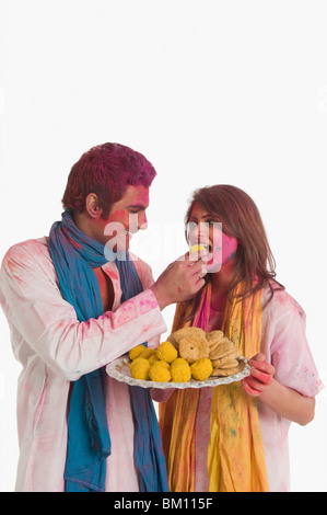 Man feeding laddu to a woman on Holi Stock Photo