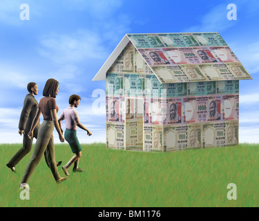 Man with women walking towards a house made from Indian rupees Stock Photo
