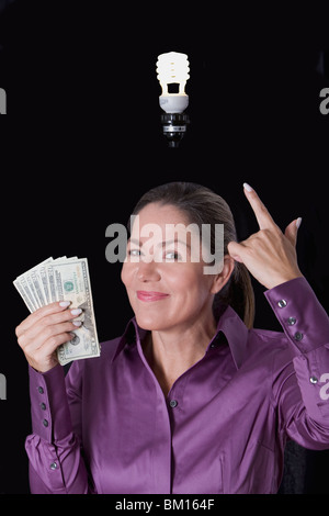 Woman holding currency notes and pointing towards a compact fluorescent light bulb Stock Photo