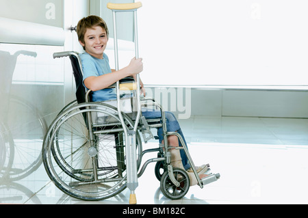 Boy holding crutch and sitting in a wheelchair Stock Photo