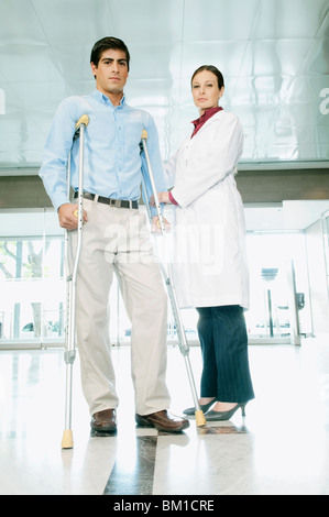 Female doctor assisting a man on crutches Stock Photo