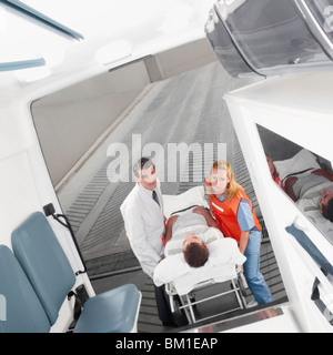 Paramedics leading a patient on a gurney into an ambulance Stock Photo
