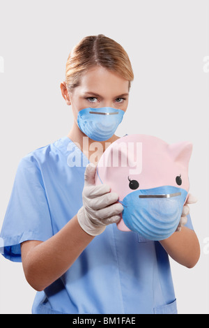 Female doctor wearing a flue mask and holding a piggy bank Stock Photo