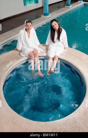 Two women sitting at the poolside with their feet soaking in water Stock Photo