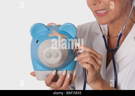 Female doctor examining a piggy bank with a stethoscope Stock Photo