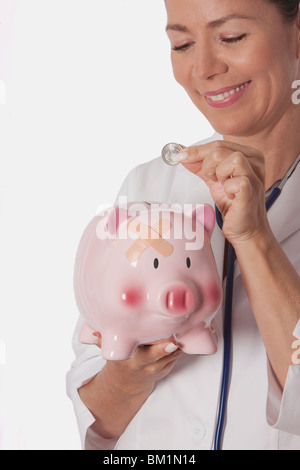 Female doctor inserting a coin into a piggy bank Stock Photo