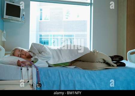 Exhausted female doctor sleeping on a patient's bed Stock Photo