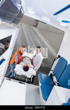 Paramedics leading a patient on a gurney into an ambulance Stock Photo