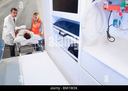 Paramedics leading a patient on a gurney into an ambulance Stock Photo