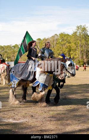 Man dressed as knight and his maiden riding their horses on jousting field while preparing for a competition Stock Photo