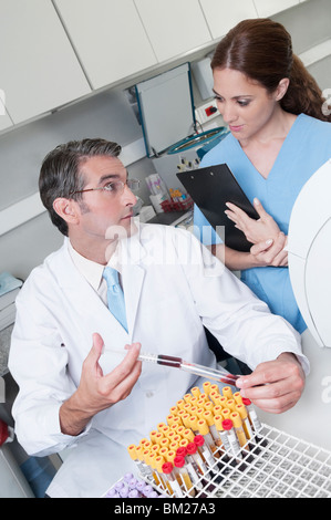 Lab technician filling blood in a test tube from a syringe and looking at his colleague Stock Photo