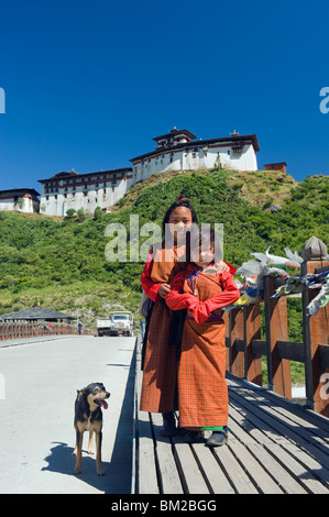 Two girls and dog on a bridge below Wangdue Phodrang Dzong, founded by the Zhabdrung in 1638, Bhutan Stock Photo