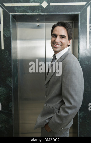 Businessman standing in front of an elevator and smiling Stock Photo
