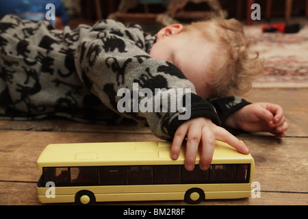 TODDLER BOY, PLAYING, TOY BUS: A two year old baby boy toddler child with curly hair playing with toy bus on the floor model released Stock Photo