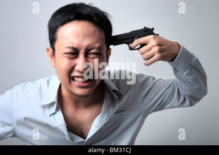 Asian businessman pointing a gun on his head Stock Photo