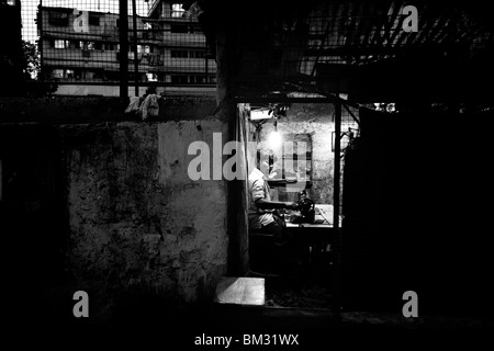 A tailor ply's his trade after dark in Kolkata India in his small street side workshop. Stock Photo