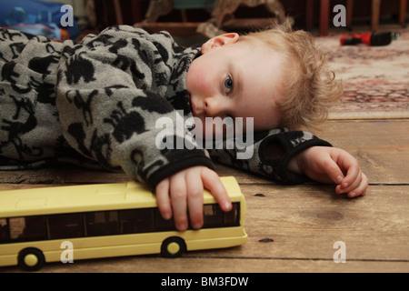 TODDLER BOY, PLAYING, TOY BUS: A two year old baby boy toddler child with curly hair playing with toy bus on the floor model released Stock Photo