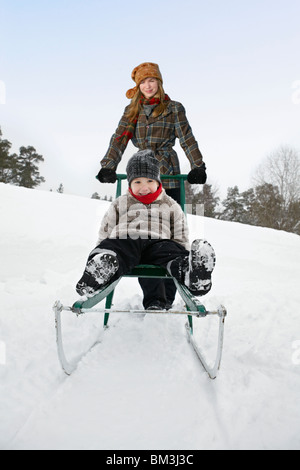 Young woman pushing boy on sled Stock Photo