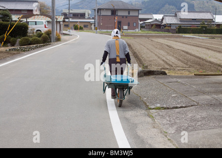 An elderly Japanese woman pulls her wheel barrow around the rural Japanese village of Seiwa, Mie Prefecture part of Taki Town Stock Photo