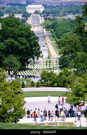 ARLINGTON, Virginia — Visitors gather at President John F. Kennedy's gravesite in Arlington National Cemetery, marked by the Eternal Flame. The view from Arlington House (the Robert E. Lee Memorial) captures the Arlington Memorial Bridge spanning the Potomac River with the Lincoln Memorial visible on the opposite shore in Washington DC. Stock Photo