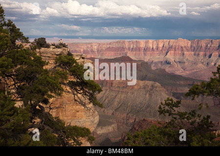 Panoramic scenic vista, Bright Angel from North rim Grand Canyon distant rain storm tiny tourist people looking out over edge of canyon wall add scale Stock Photo