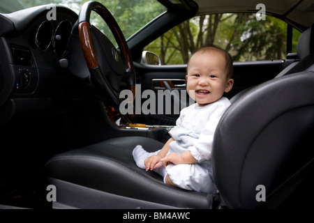 Asian baby boy sitting in driver's seat Stock Photo