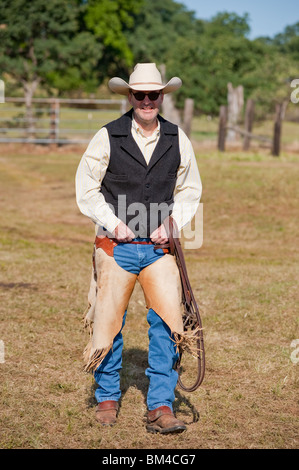 Cowboy walking to his horse with bridle and chaps Stock Photo